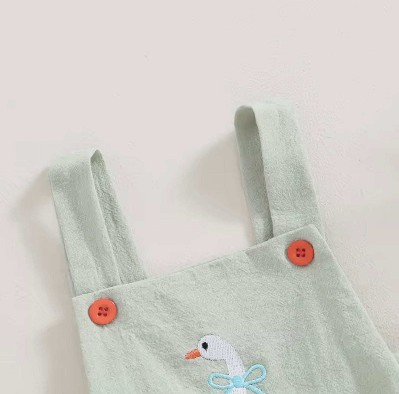Light green overalls with orange buttons and a duck design on a white background